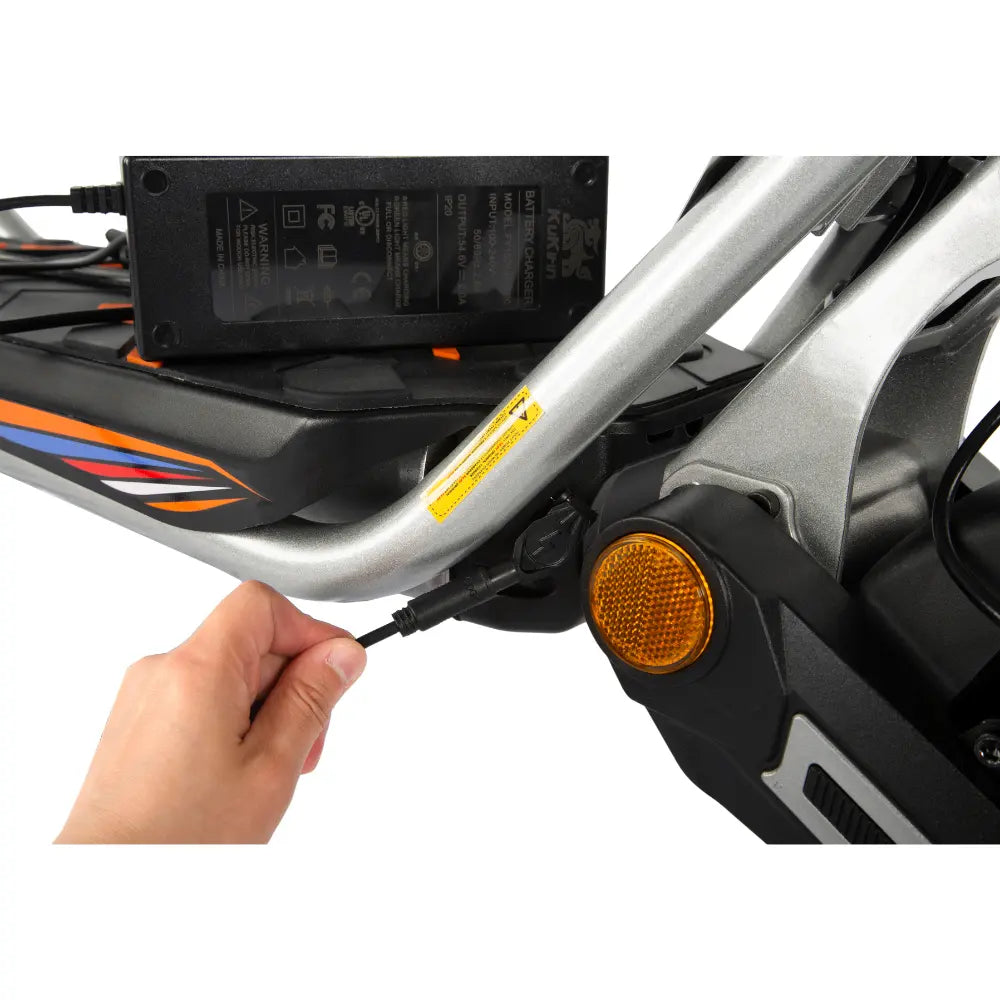 Charging the KuKirin A1 scooter: hand plugging the charger into the charging port, showing battery charging setup