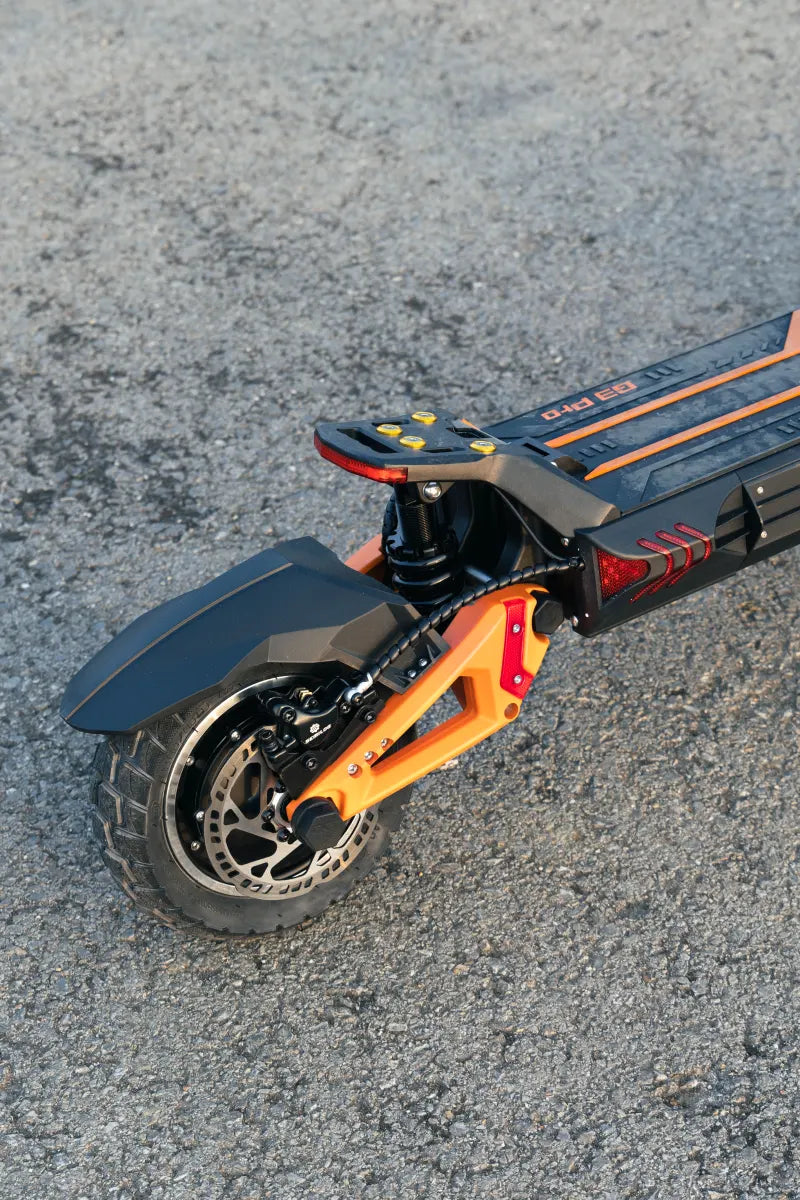 KuKirin G3 Pro electric scooter rear wheel close-up, showing disc brake, shock absorber, and orange frame on asphalt road