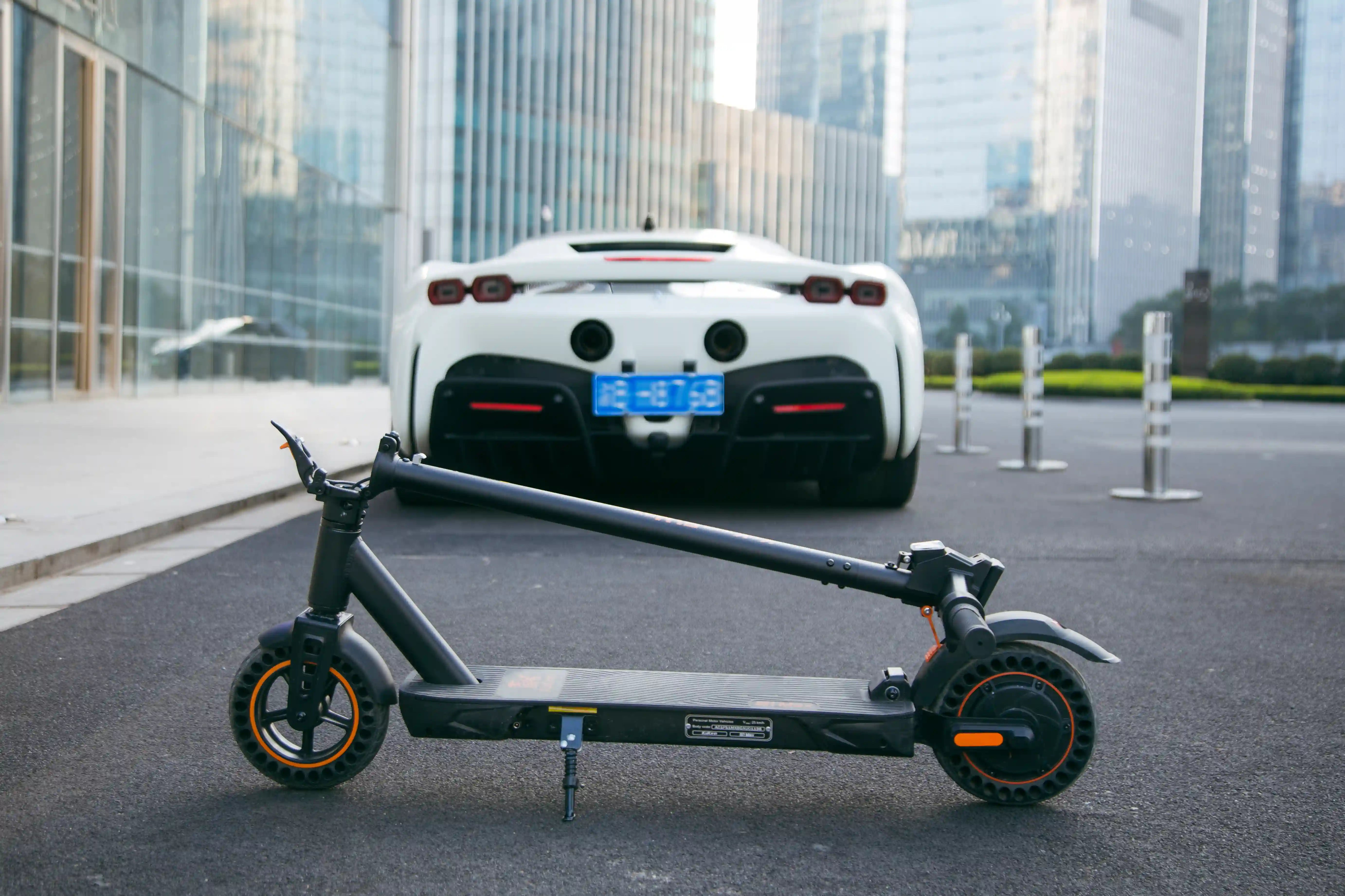 KuKirin S1 Max electric scooter parked on urban road, modern city buildings and sports car in background.